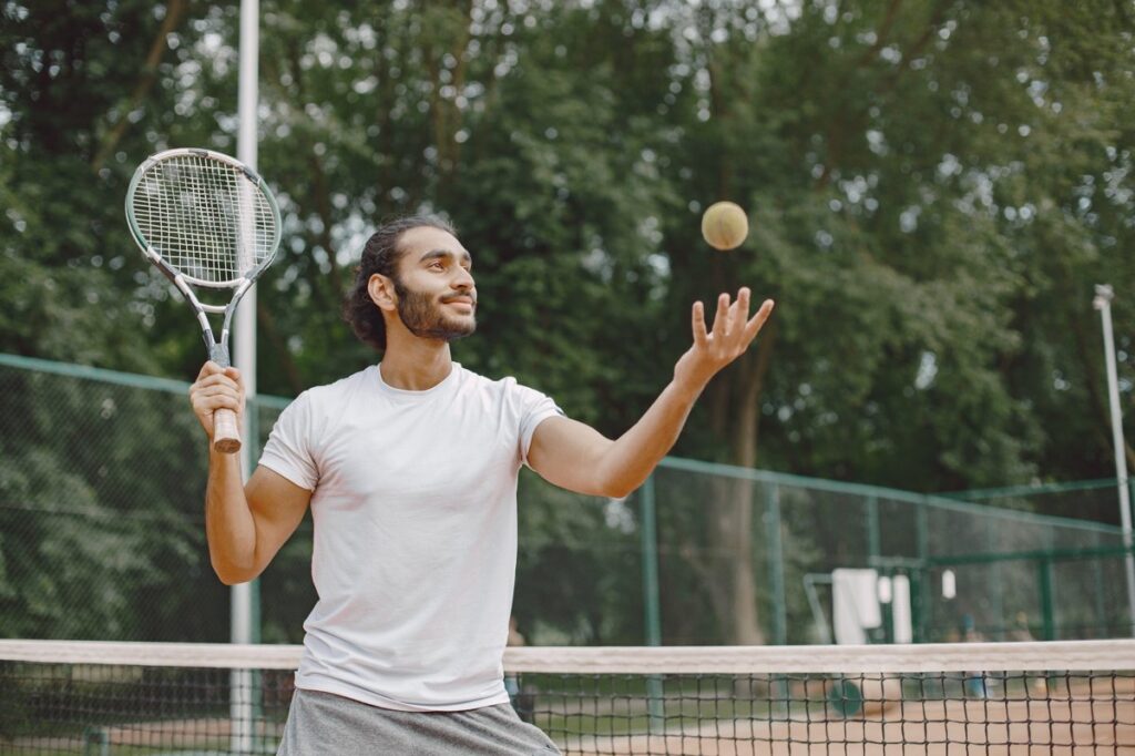 Pemain tenis pria sedang bersiap melakukan teknik servis di lapangan luar ruangan
