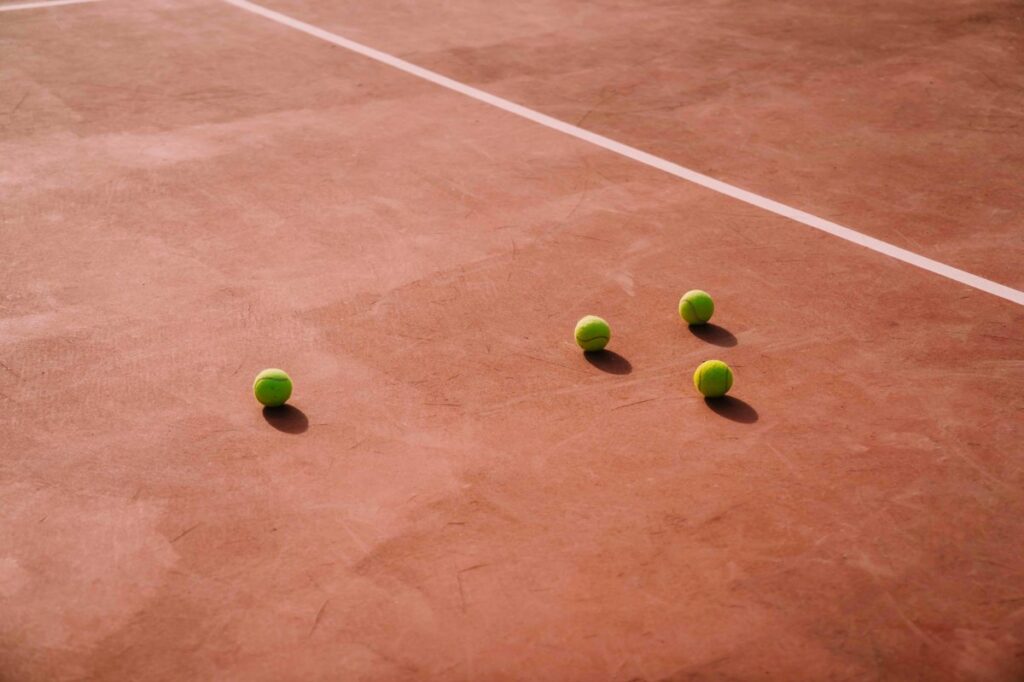 Empat bola tenis di atas lapangan tanah liat berwarna merah