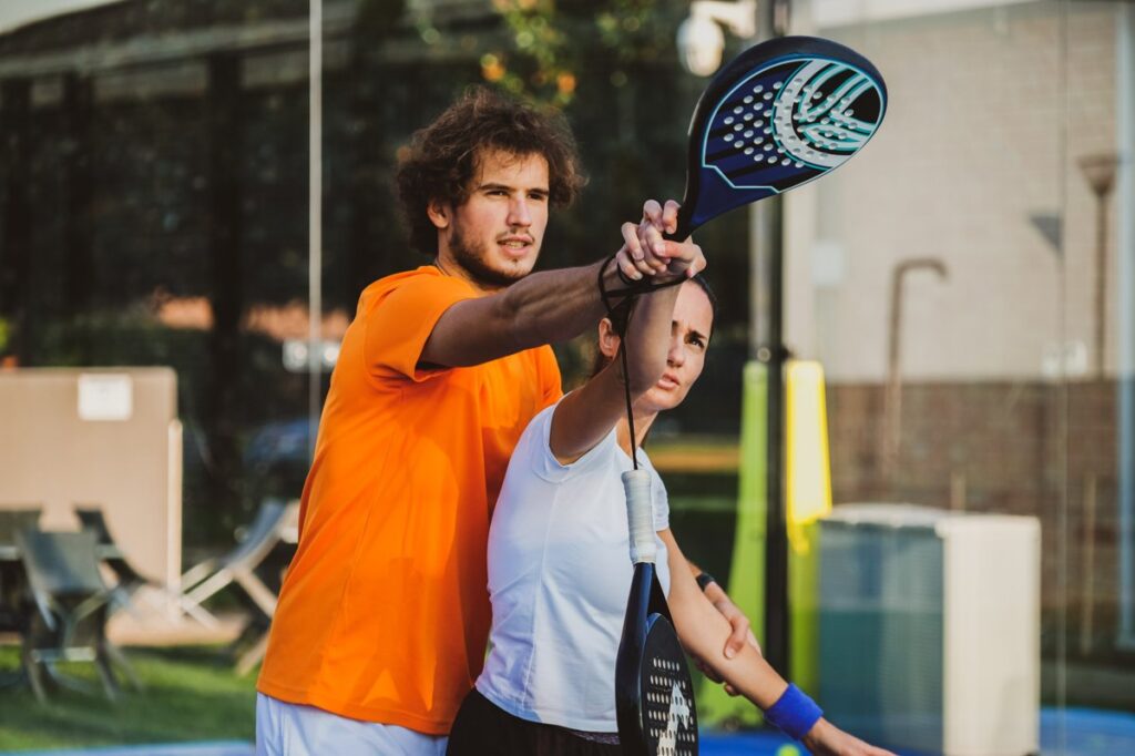 Pelatih padel sedang mengajarkan teknik servis kepada pemain pemula di lapangan outdoor