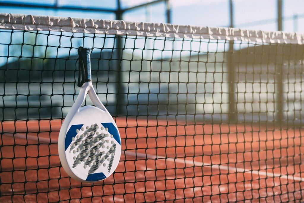 Raket padel tergantung di net dengan latar belakang lapangan tanah merah
