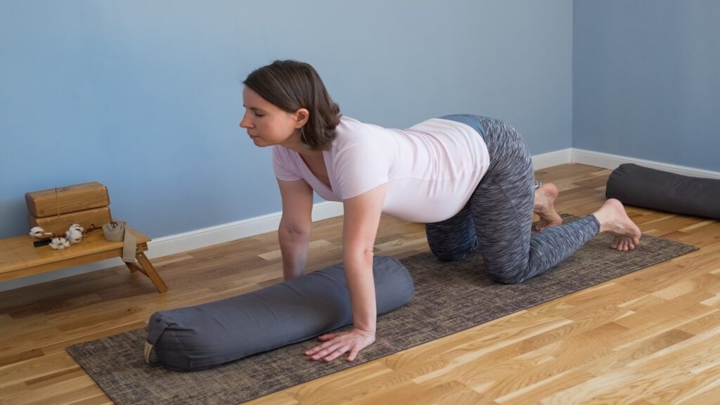 Ibu hamil melakukan prenatal yoga dengan bolster di rumah