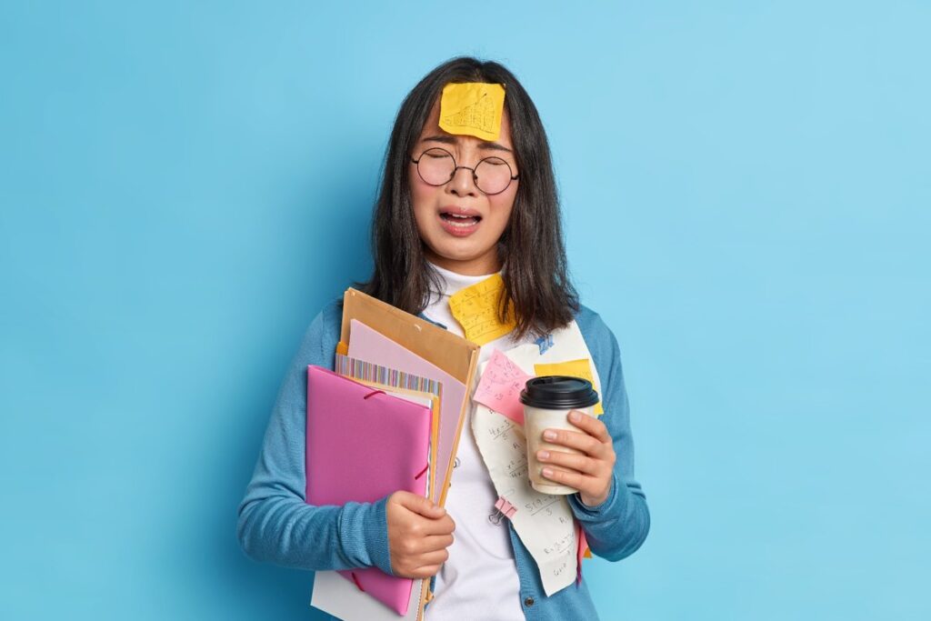 Wanita Asia kelelahan membawa banyak dokumen sambil memegang kopi, mencerminkan gaya hidup sibuk