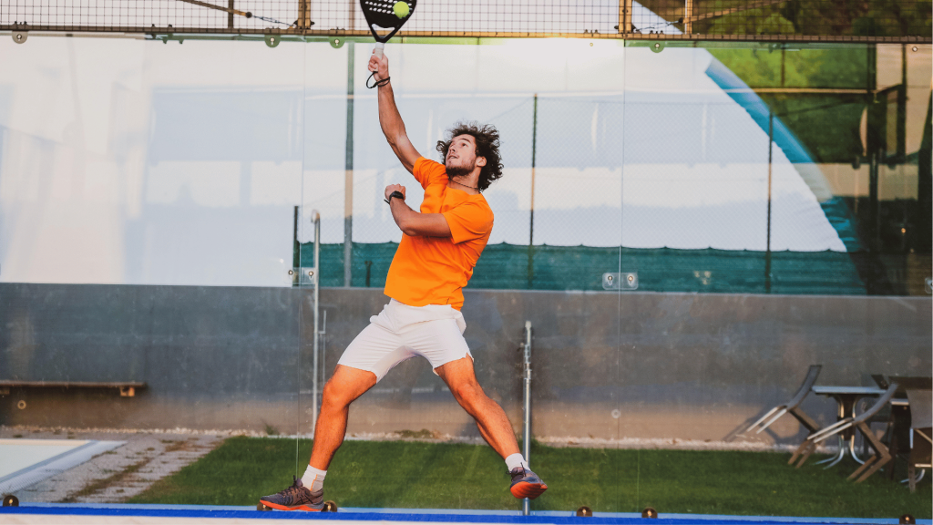 Seorang pria memukul bola tenis di lapangan padel